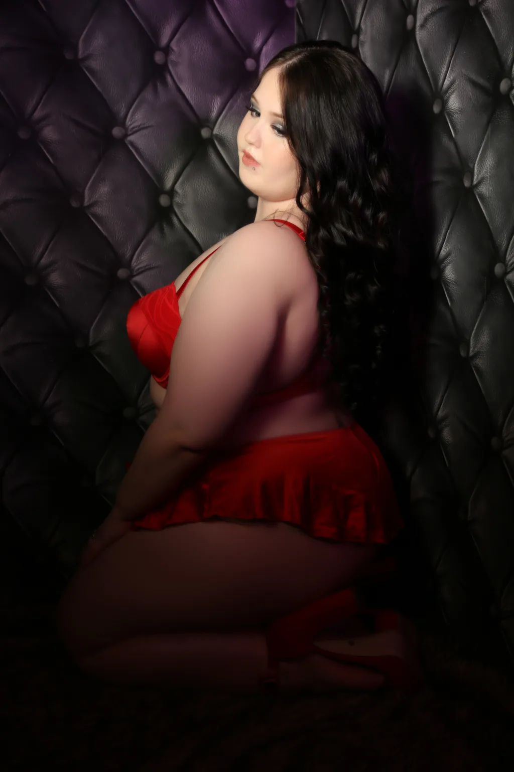boudoir photography studio with woman in red lingerie posing on her knees looking down