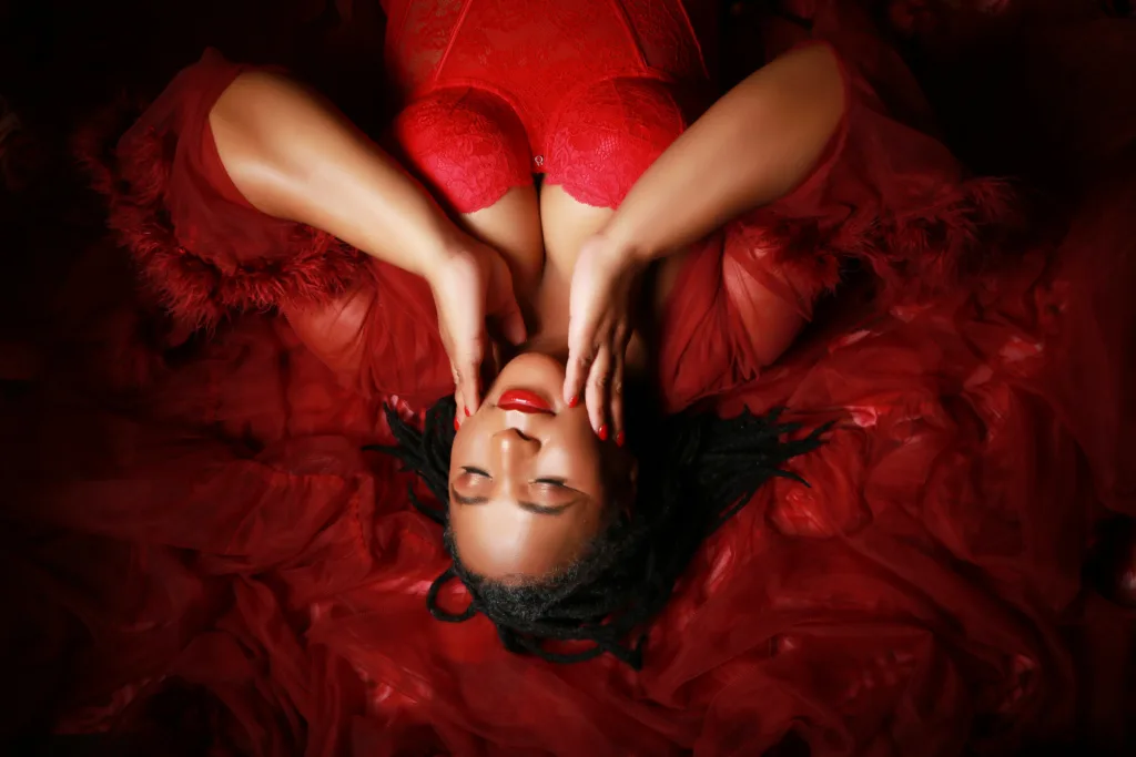 Woman posing on her back in a boudoir photography studio in Manchester with long red gown