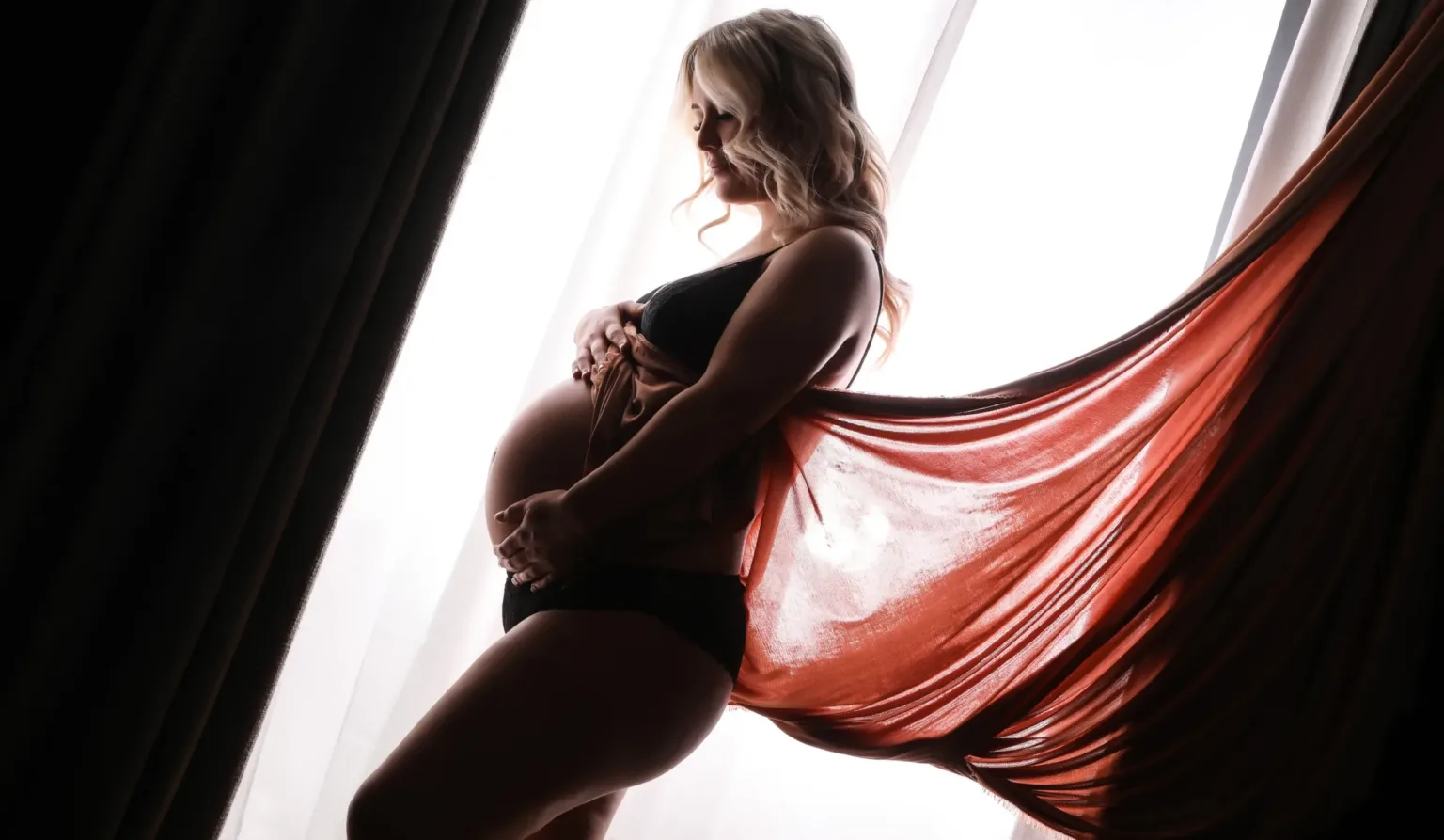 pregnant woman posing for a maternity photoshoot in front of white lights and red gown