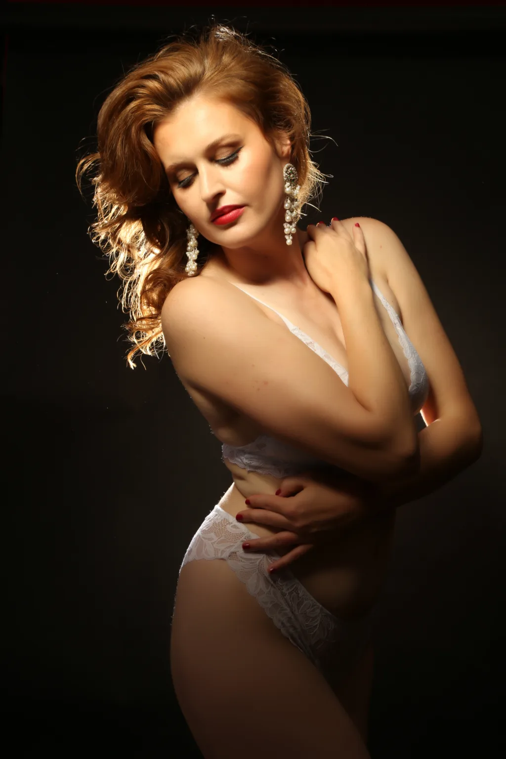 boudoir photoshoot with woman in white lingerie posing in front of dark wall and studio lights