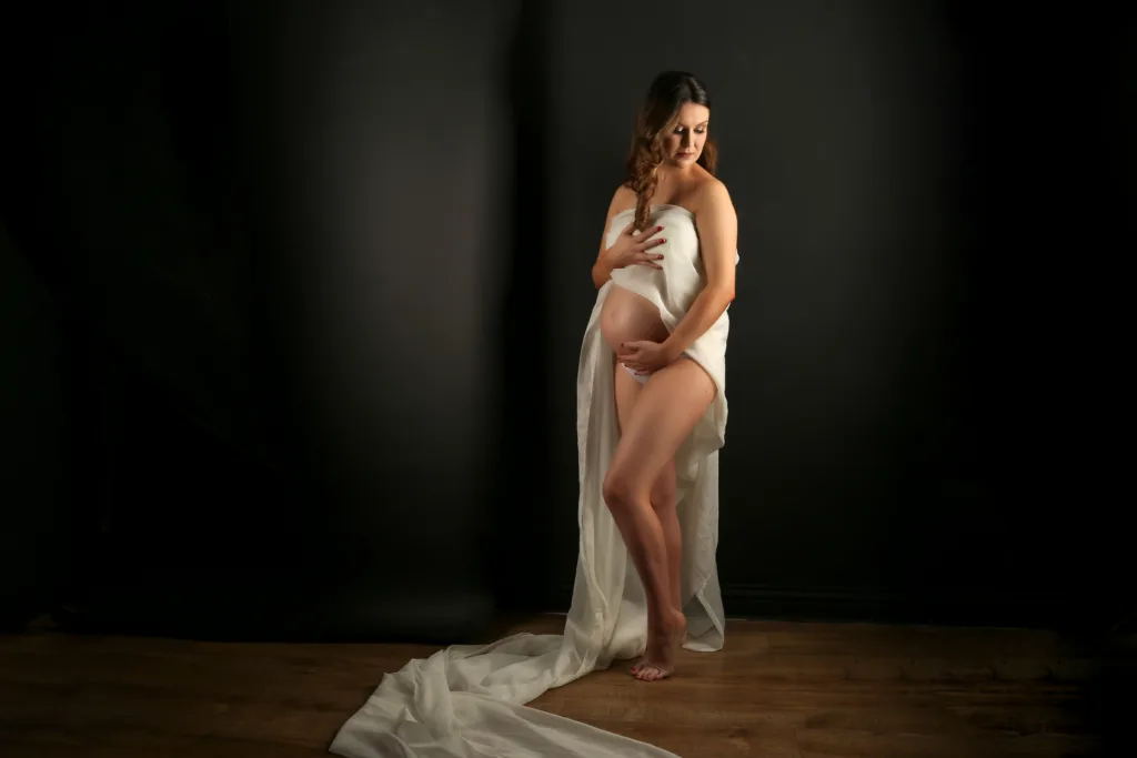 pregnant woman posing in a maternity photography studio in front of black walls