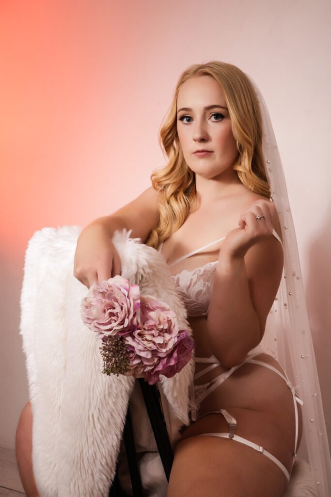 woman posing for a pre-wedding photoshoot on a chair in front of white wall with pink studio lights